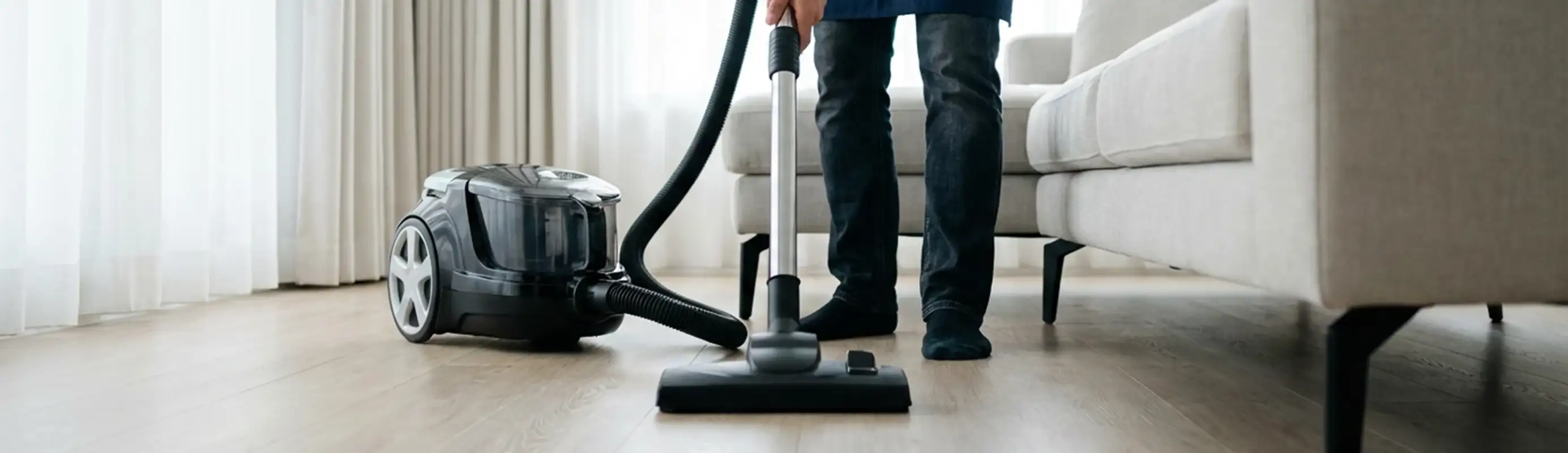 Professional house cleaner vacuuming a living room floor with a canister vacuum cleaner, San Jose, CA.
