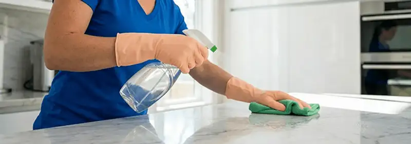 Maid service worker spraying and wiping a kitchen countertop with a microfiber cloth for sanitizing, San Jose, CA.