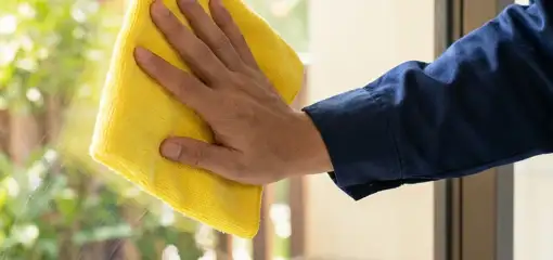 House cleaner wiping a glass window with a yellow microfiber cloth for streak-free cleaning, San Jose, CA.